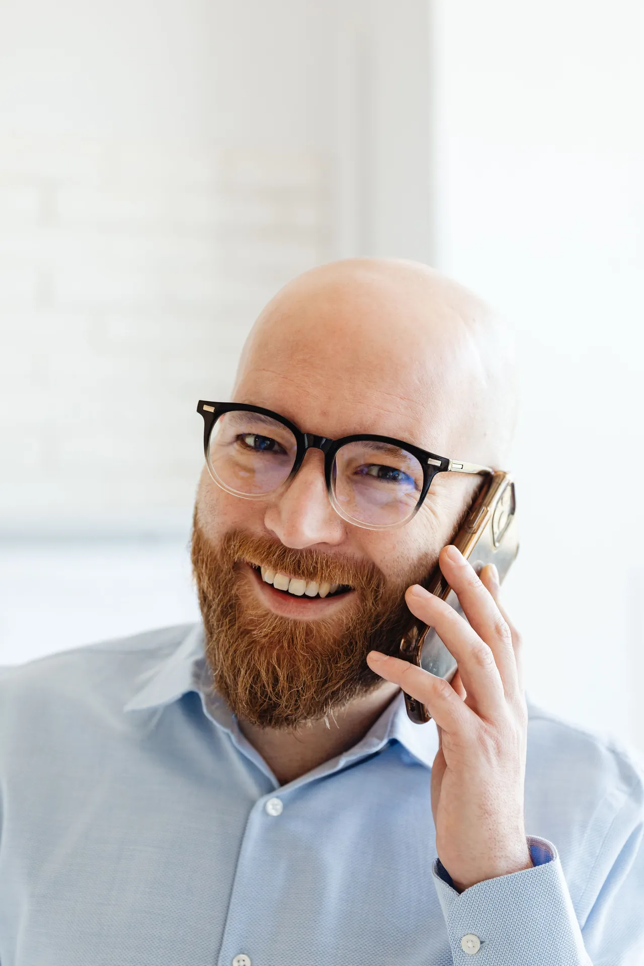 Leende man med skägg och glasögon som pratar i mobiltelefon