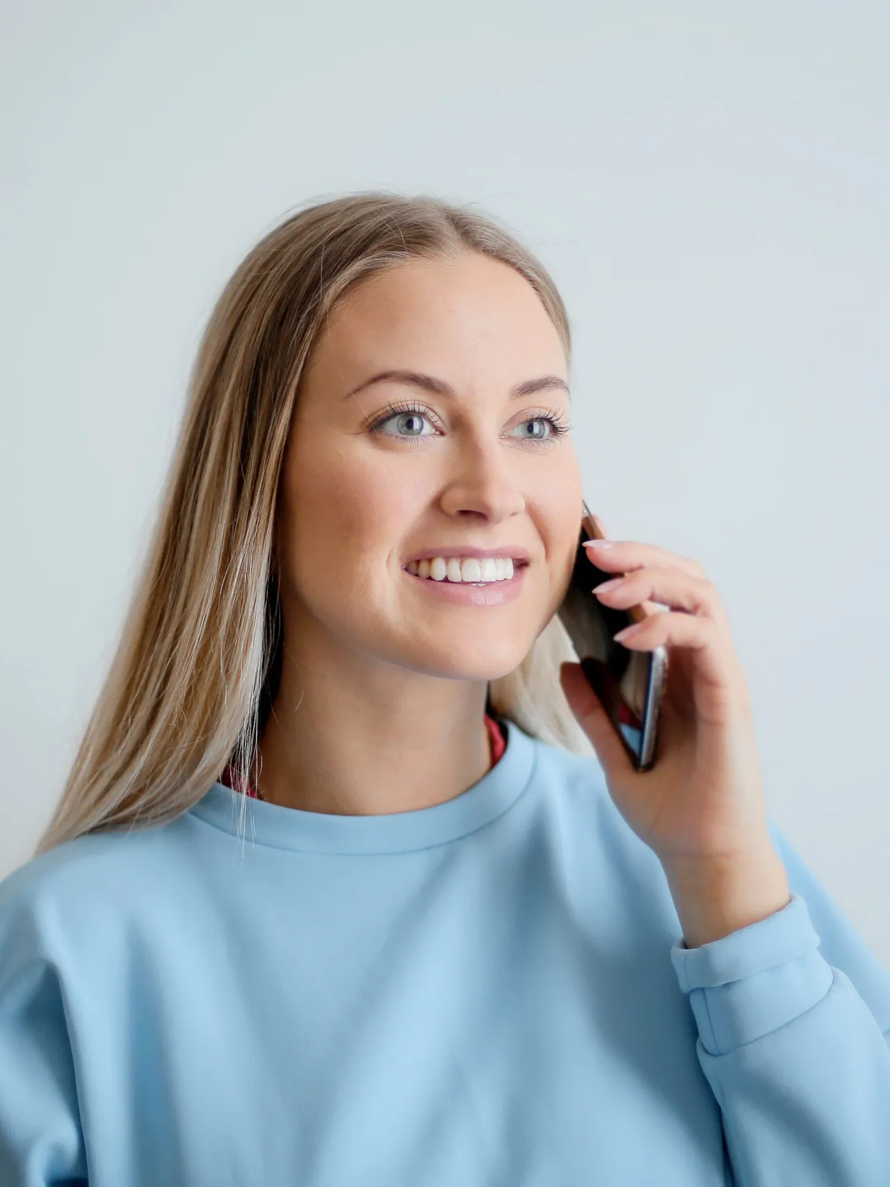 Leende kvinna med långt ljust hår och ljusblå tröja som pratar i mobiltelefon