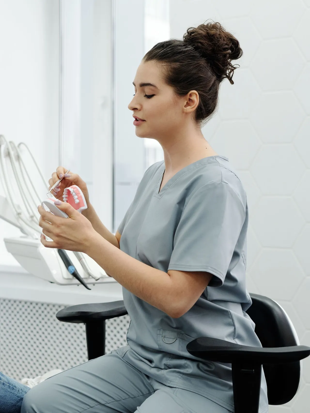 Tandhygienist i grå arbetskläder visar hur man borstar på en tandmodell